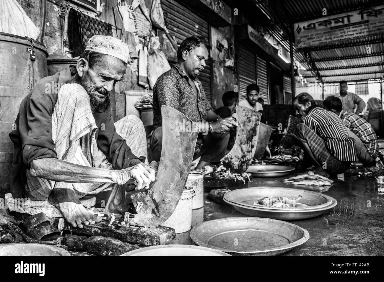 De pauvres vieillards coupent du poisson dans un marché aux poissons local à Barishal, au Bangladesh. Banque D'Images