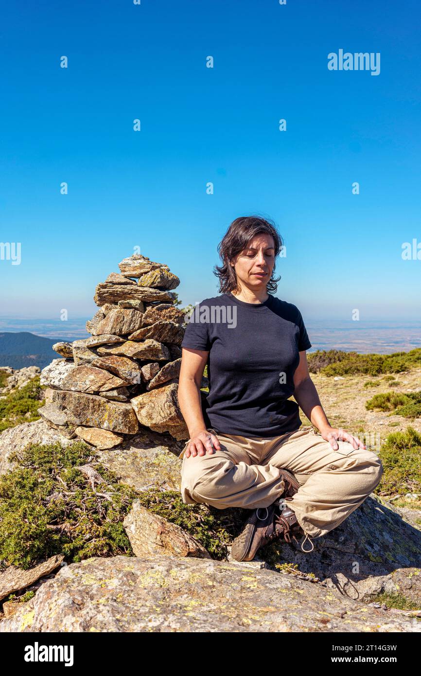 Femme d'âge moyen assise à côté d'un jalon en position facile pour un exercice de méditation au milieu de la nature. Banque D'Images