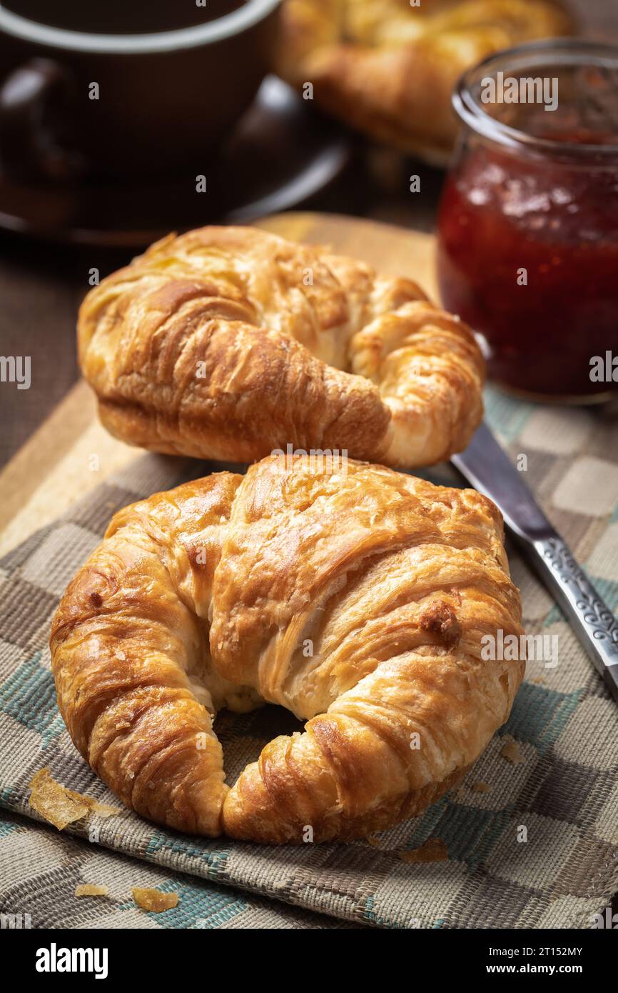 Deux croissants avec des conserves de fraises et une tasse de café sur une table en bois rustique Banque D'Images