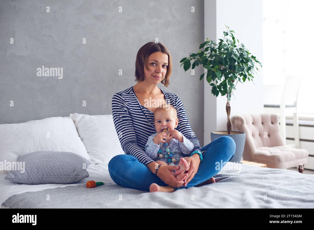 mère avec un bébé de 8 mois assis sur un lit à la maison. Banque D'Images