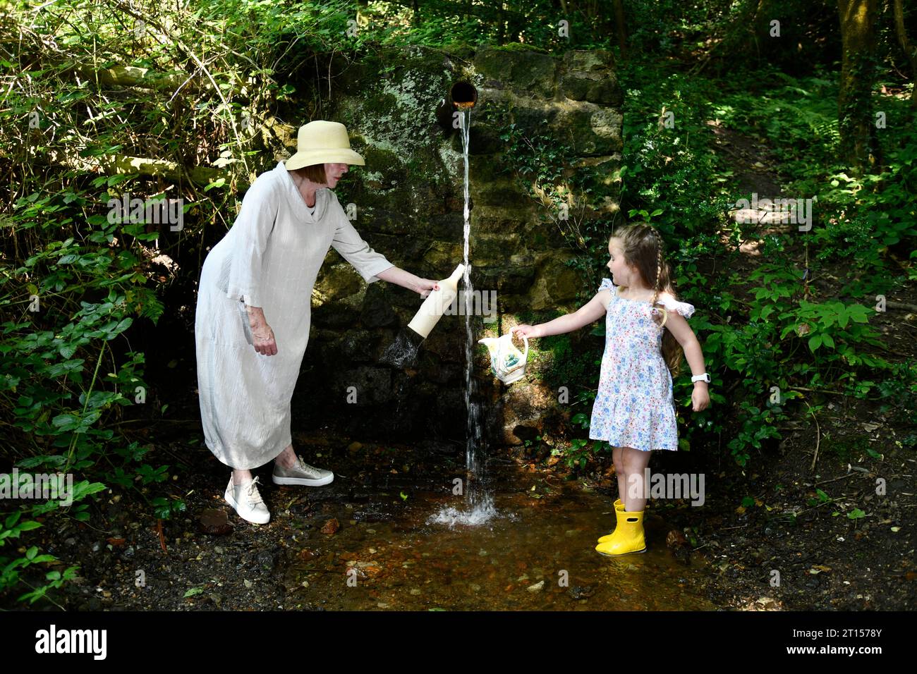 Femme et enfant recueillant l'eau de source fraîche de la conduite d'eau de Mine Spout réputée pour être de l'eau pure, Spout Lane, Benthall, Shropshire Banque D'Images