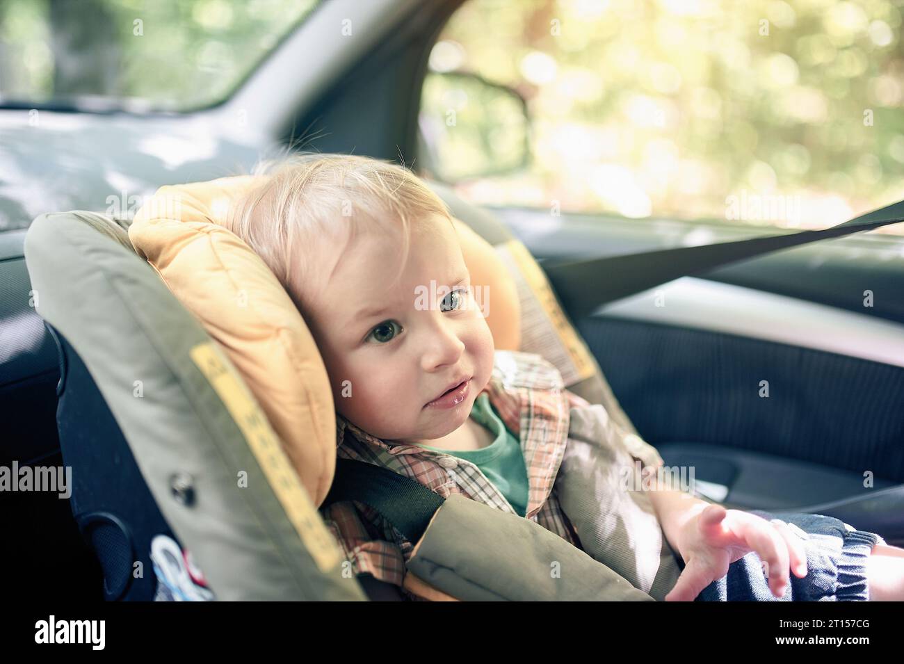 Portrait de joli garçon en bas âge de 1 ans assis dans le siège de sécurité de voiture monté dans le siège avant. Sécurité du transport des enfants. Étiquettes d'avertissement sur le cha Banque D'Images