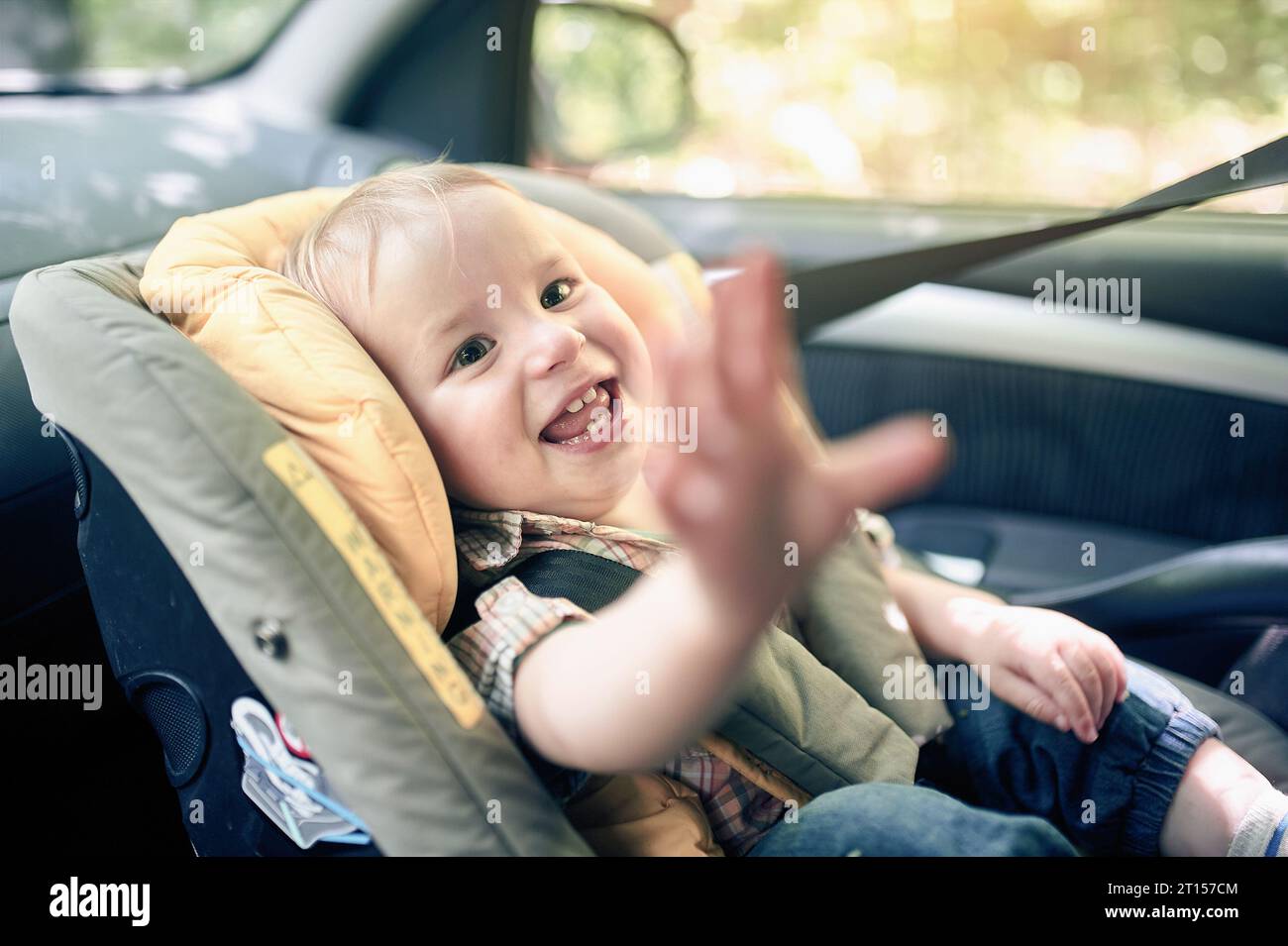 Portrait de joli garçon en bas âge de 1 ans assis dans le siège de sécurité de voiture monté dans le siège avant. Sécurité du transport des enfants. Étiquettes d'avertissement sur le cha Banque D'Images