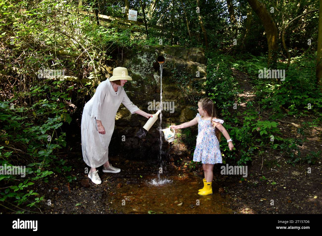 Femme et enfant recueillant l'eau de source fraîche de la conduite d'eau de Mine Spout réputée pour être de l'eau pure, Spout Lane, Benthall, Shropshire Banque D'Images