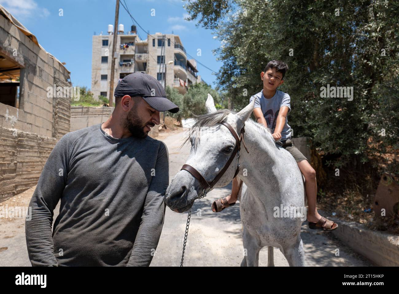 Bayt Surik, Palestine – 19 juin 2023 : Young Arab Man touche un beau cheval blanc et avec Sad Looking Boy sur le dessus de lui Banque D'Images