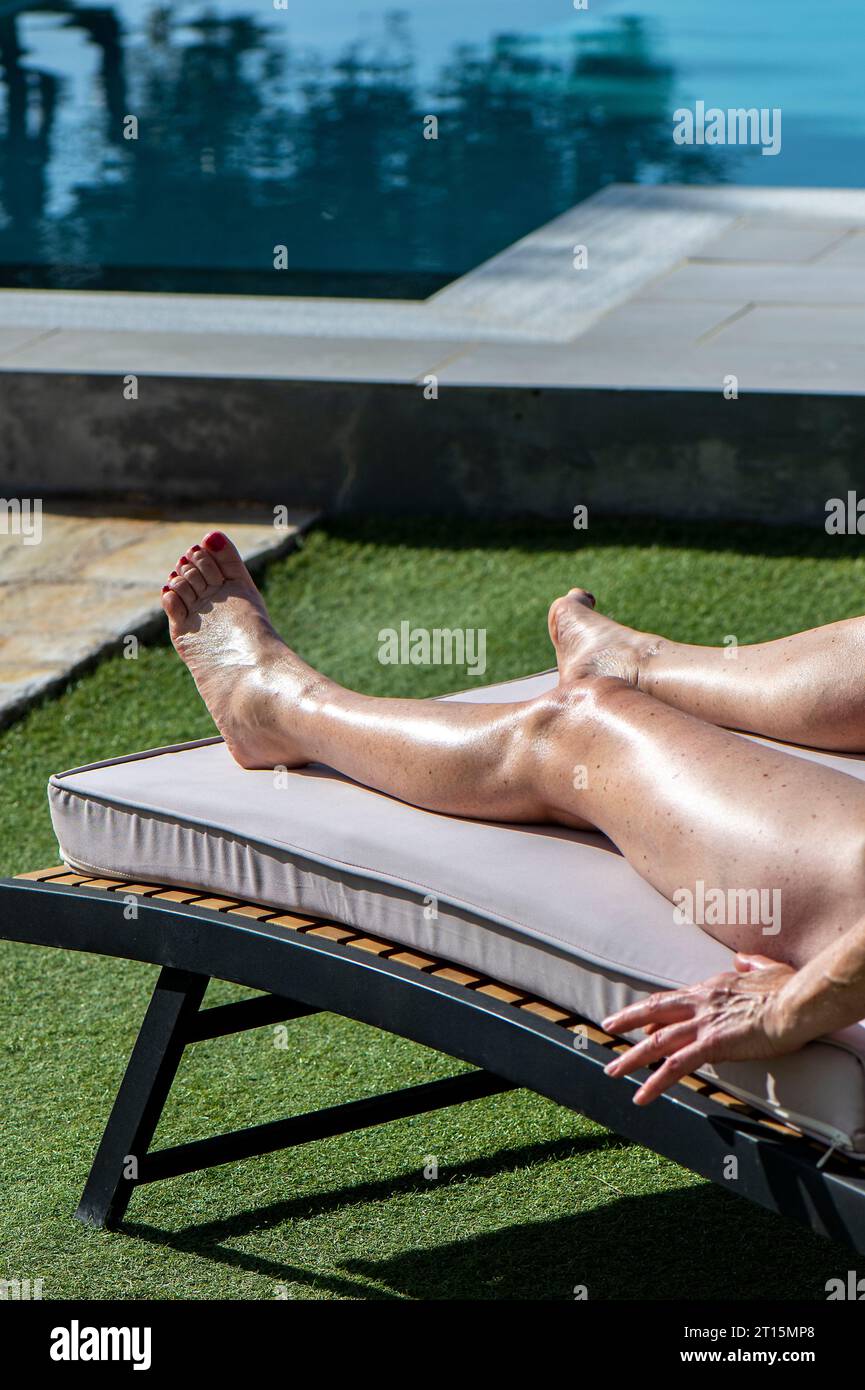 lady bronzer ou bronzer à côté d'une piscine en vacances dans une villa en grèce. gros plan des jambes féminines bronzant au soleil à côté de la piscine se détendre. Banque D'Images