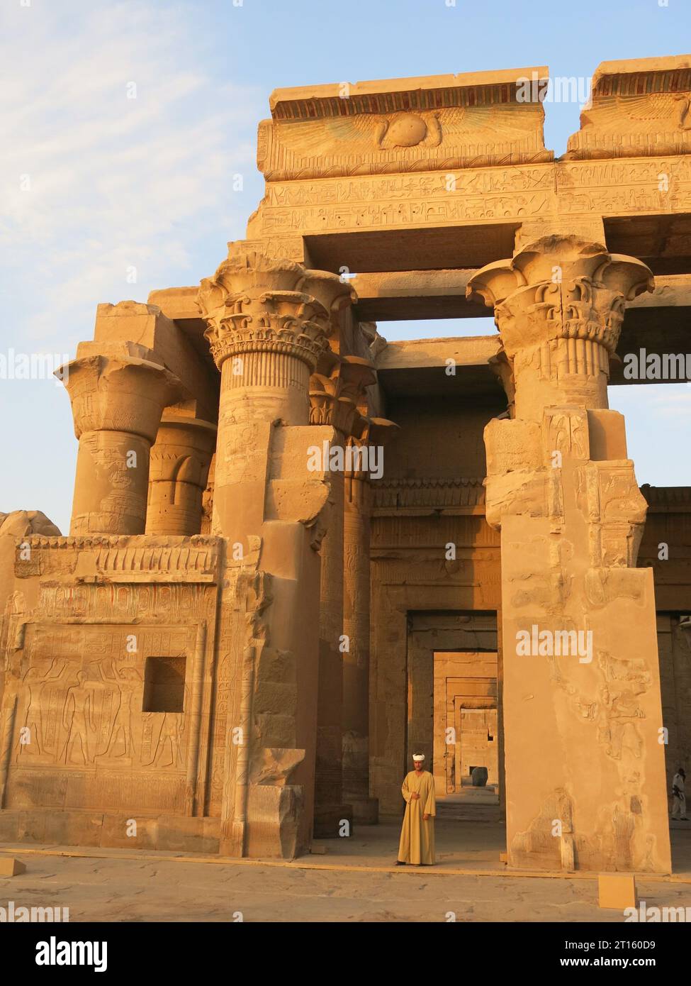 Homme en robe égyptienne se tient devant les anciens piliers en forme de papyrus du Temple de Kom Ombo, brillant dans le soleil du soir. Banque D'Images