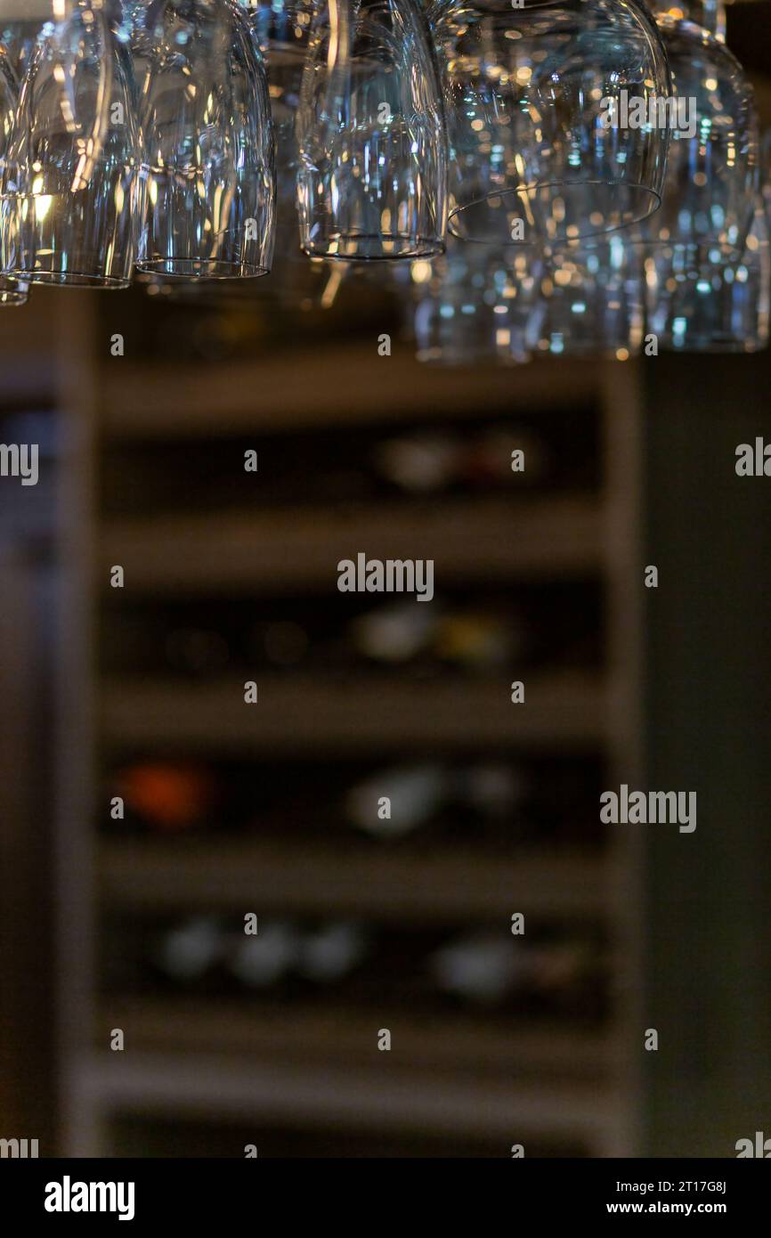 Nettoyez les verres à vin suspendus au-dessus du comptoir du bar sur fond flou avec une étagère avec des bouteilles de vin Banque D'Images