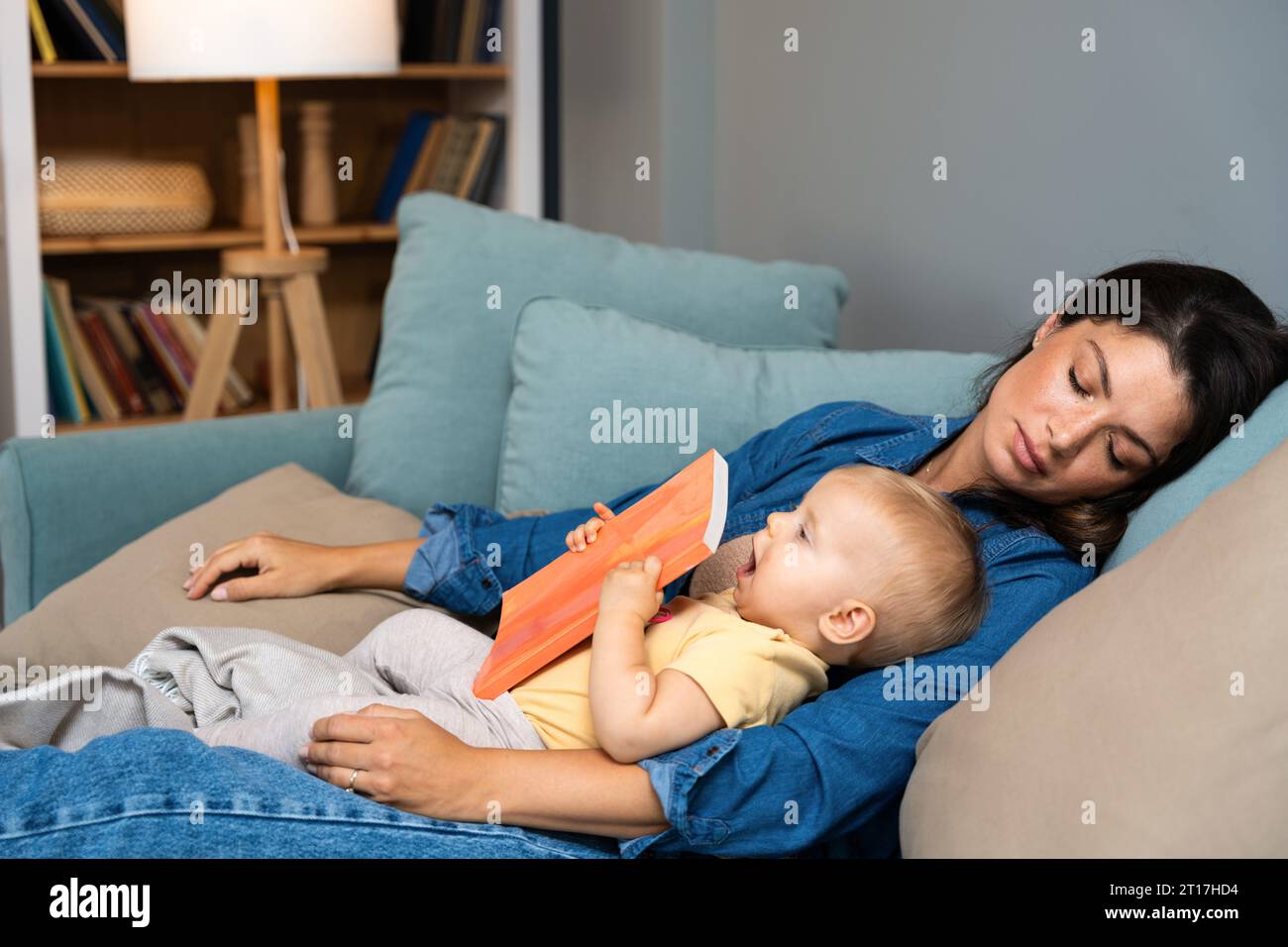 La jeune mère s'est endormie après avoir lu un livre d'histoire de conte de fées à son bébé. Maman fatiguée dormant avec son enfant sur ses genoux a essayé de lire à son enfant dans t Banque D'Images