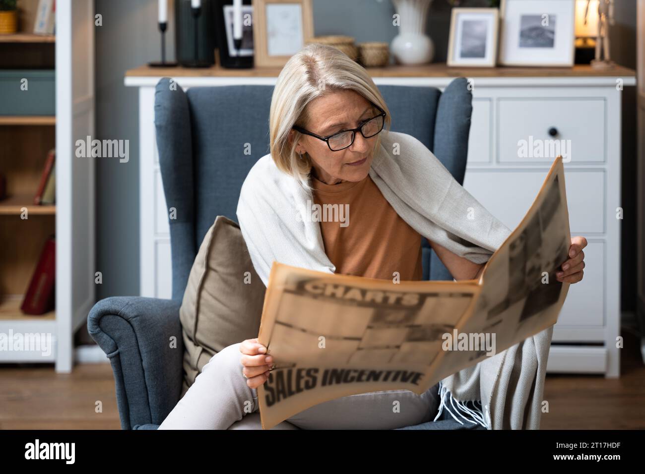 Femme âgée assise à son fauteuil confortable à sa maison lisant le journal, suivant les nouvelles. Âge moyen retraité femelle lire l'information vieux sch Banque D'Images