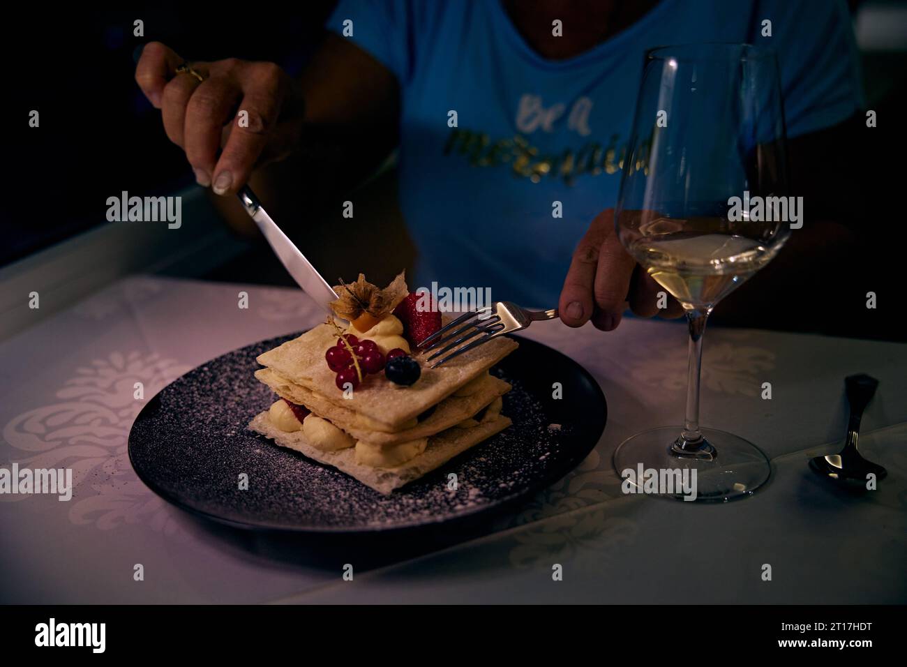 Millefeuille dessert sucré avec fraises sur table avec glasse de vin blanc. Une femme mange un dessert dans un restaurant. Banque D'Images