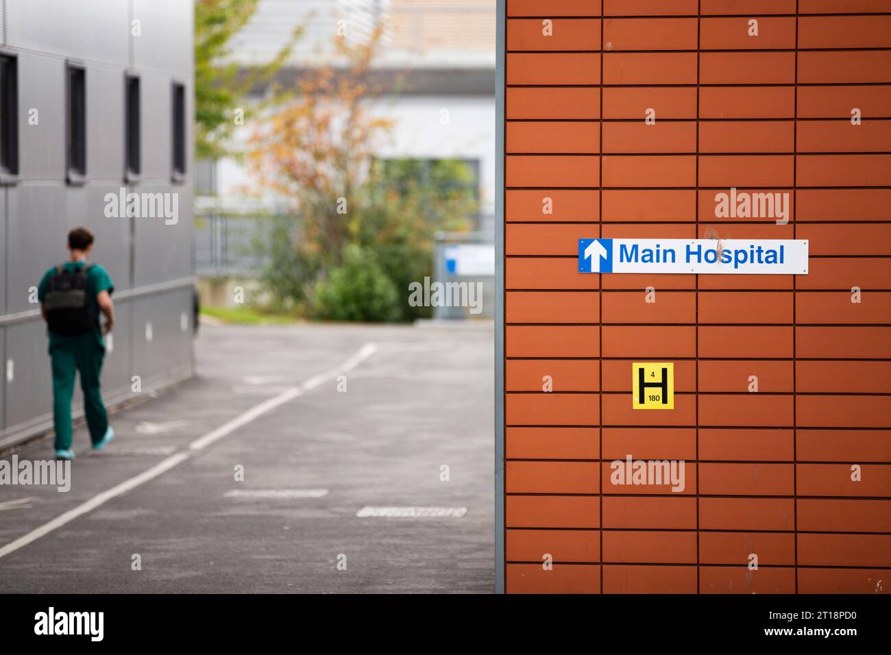 Vert uniforme homme / médecin / professionnel de la santé ou consultant entrant dans l'hôpital principal et marchant devant le signe à l'hôpital Exeter R D & E. Banque D'Images