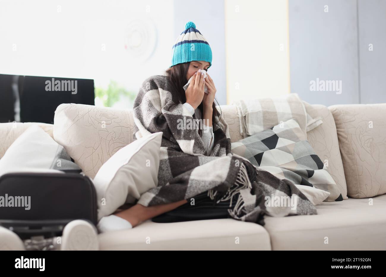 femme réfrigérée sur le canapé dans une couverture et chapeau tient le mouchoir Banque D'Images