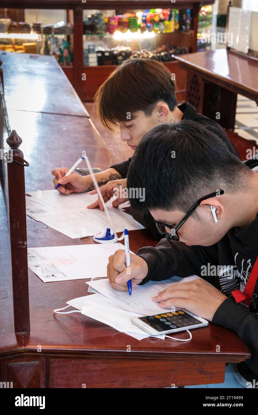 Ho Chi Minh, Vietnam. Bureau de poste de l'ère coloniale française. Jeunes hommes écrivant. Banque D'Images