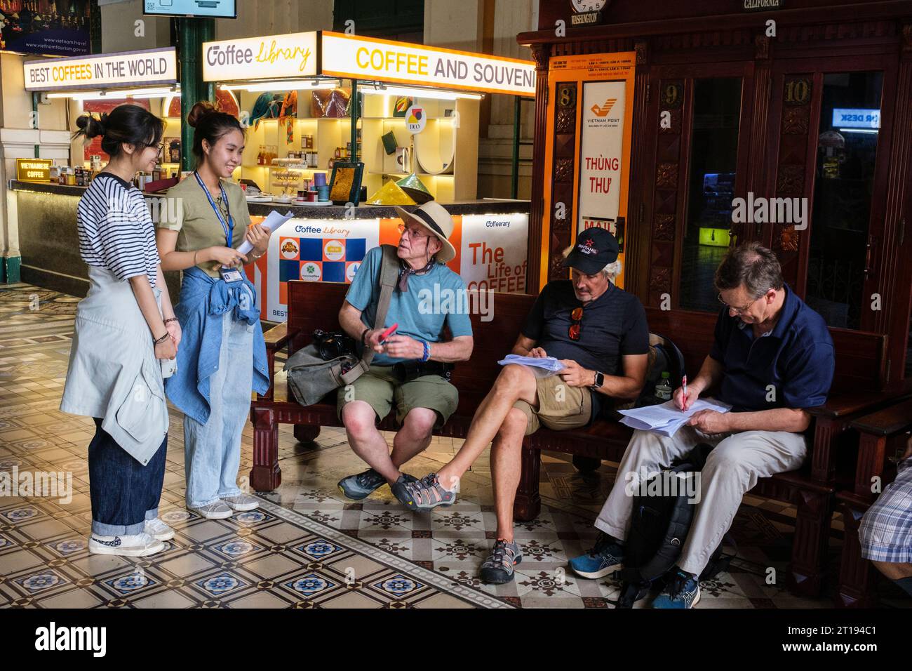 Ho Chi Minh, Vietnam. Bureau de poste de l'ère coloniale française. Jeunes femmes vietnamiennes menant une enquête auprès des touristes. Banque D'Images