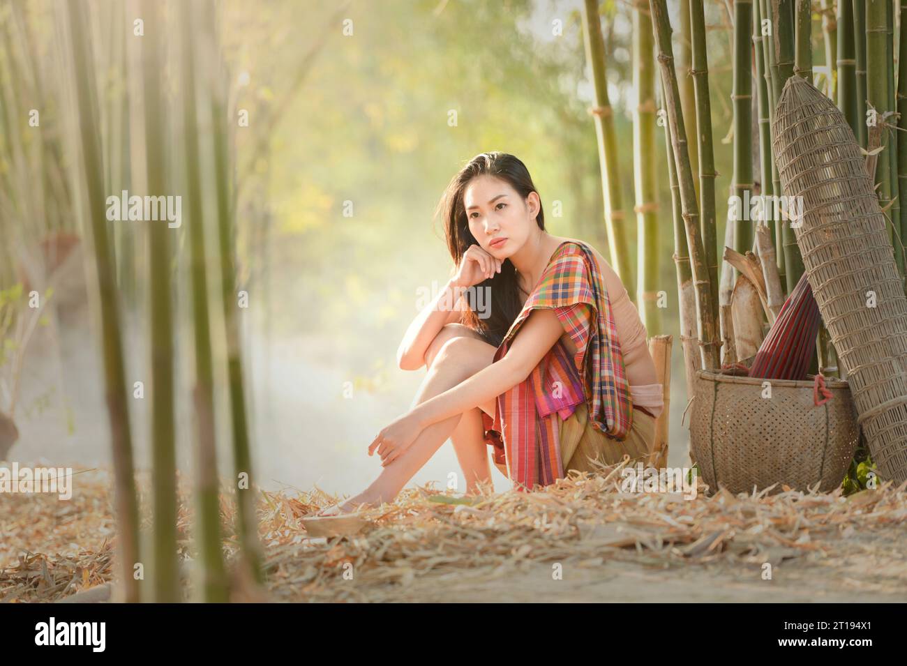 Femme réfléchie assise dans un jardin parmi les plantes de bambou, Thaïlande Banque D'Images