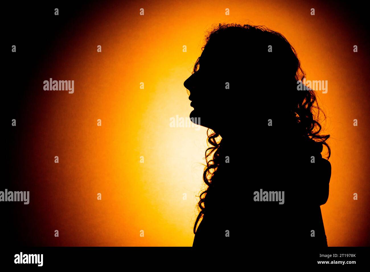 Silhouette d'une jeune femme avec de longs cheveux bouclés sur un fond orange Banque D'Images