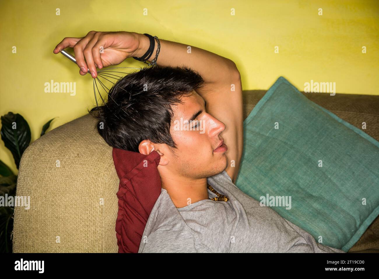 Un homme allongé sur un canapé avec un masseur de tête dans sa main.photo d'un jeune et bel homme se détendant sur un canapé avec un masseur de tête en main Banque D'Images