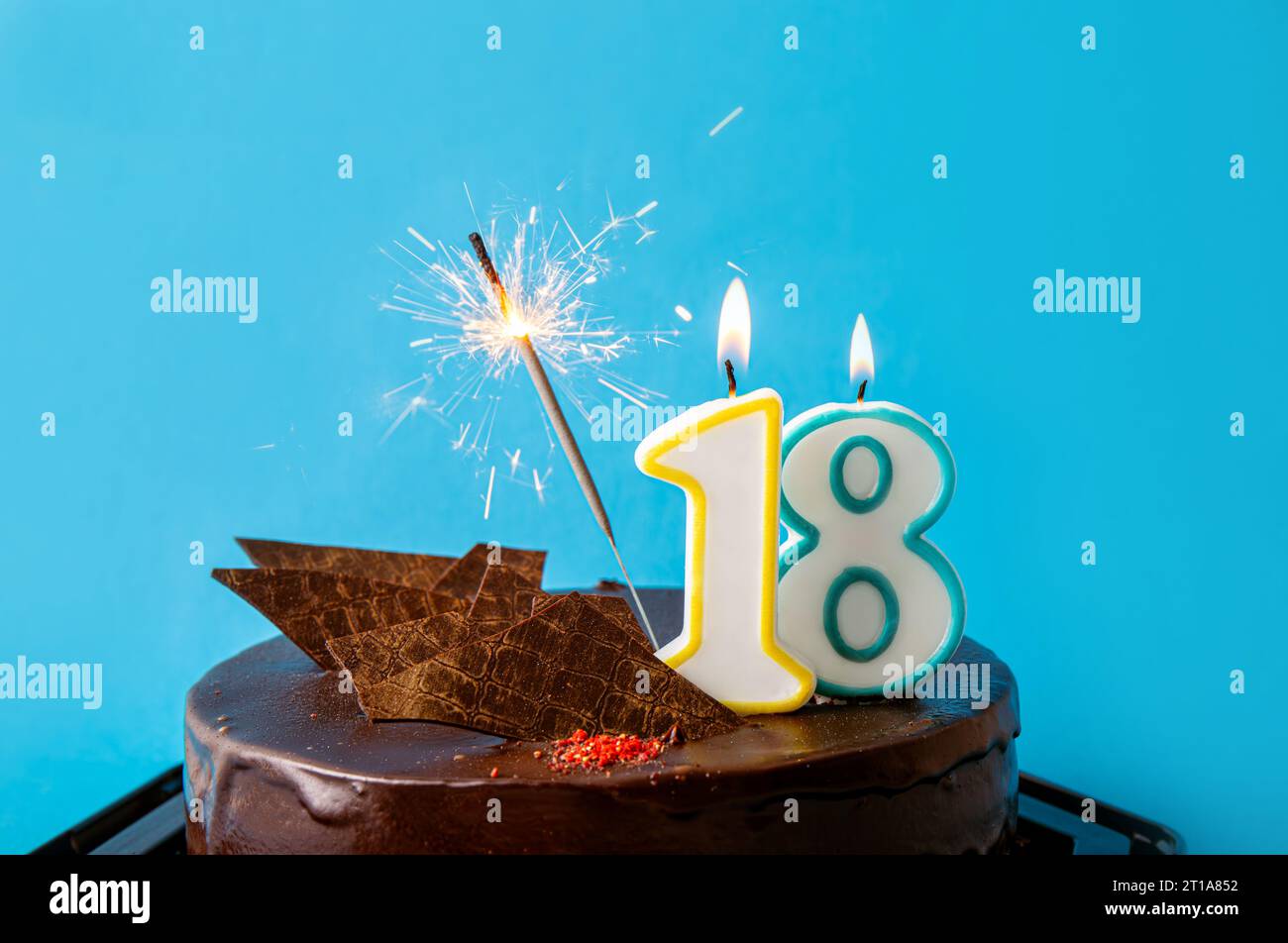 Bougie d'anniversaire numéro 18 brûlant sur le gâteau, étincelles étincelantes volent. Le concept de célébration du dix-huitième anniversaire ou anniversaire. Beaucoup d'espace de copie sur bleu Banque D'Images