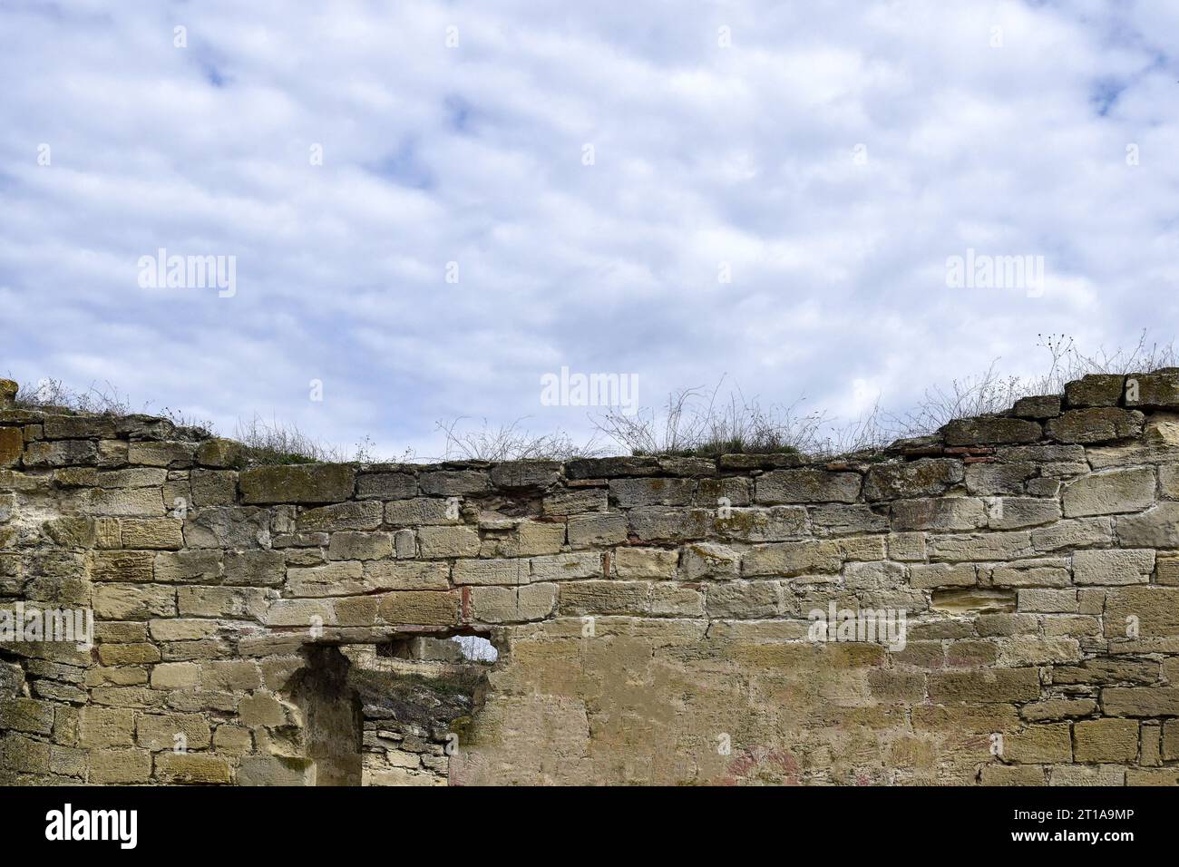 Un vieux mur d'un ancien bâtiment en pierre détruit par le temps avec de l'herbe sèche sur le fond d'un ciel nuageux. Espace de copie. Mise au point sélective. Banque D'Images