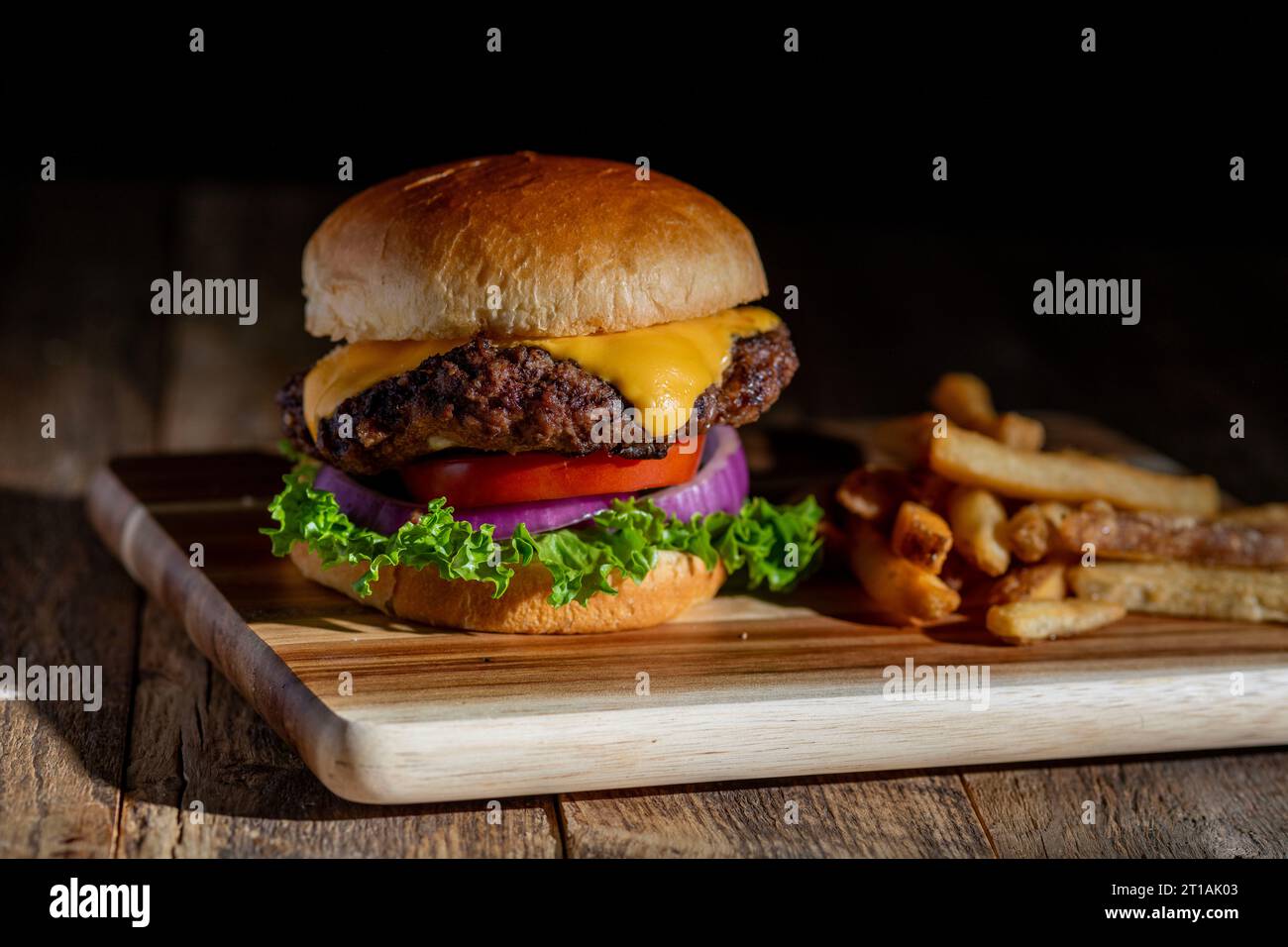 Un Cheeseburger grillé frais avec fromage fondu, laitue, tomate et oignons sur un brioche. Côté frites avec Banque D'Images