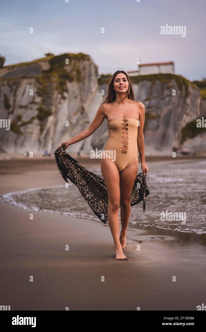 Une femme brune avec un maillot de bain et un paréo marchant sur la plage en été Banque D'Images