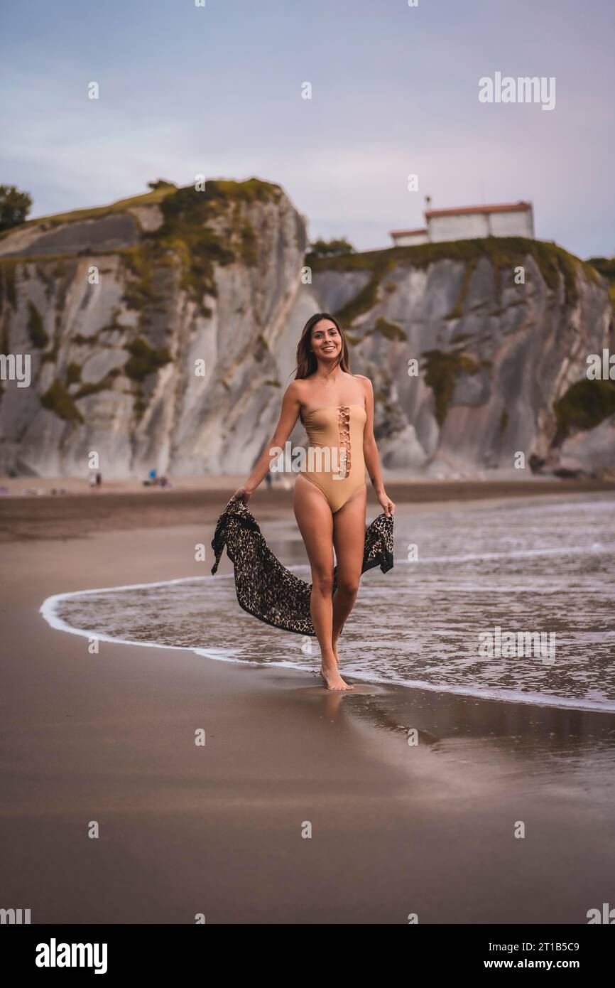 Une femme brune avec un maillot de bain et un paréo marchant sur la plage en été Banque D'Images