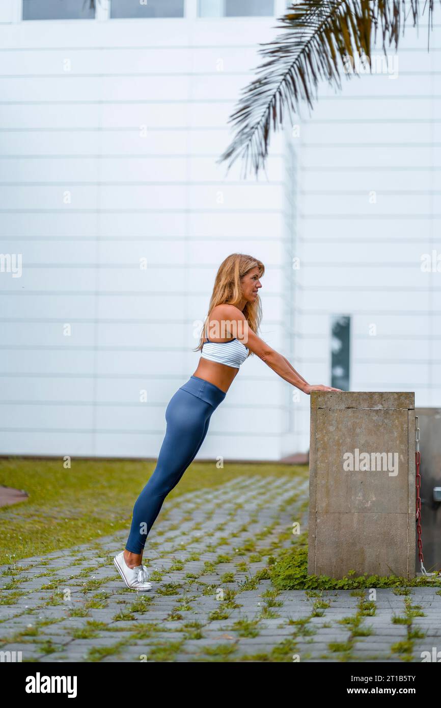 Séance de fitness et de yoga avec une jeune instructrice blonde caucasienne vêtue d’une tenue décontractée avec Maya bleue et un T-shirt blanc. Réalisation d'étirements Banque D'Images
