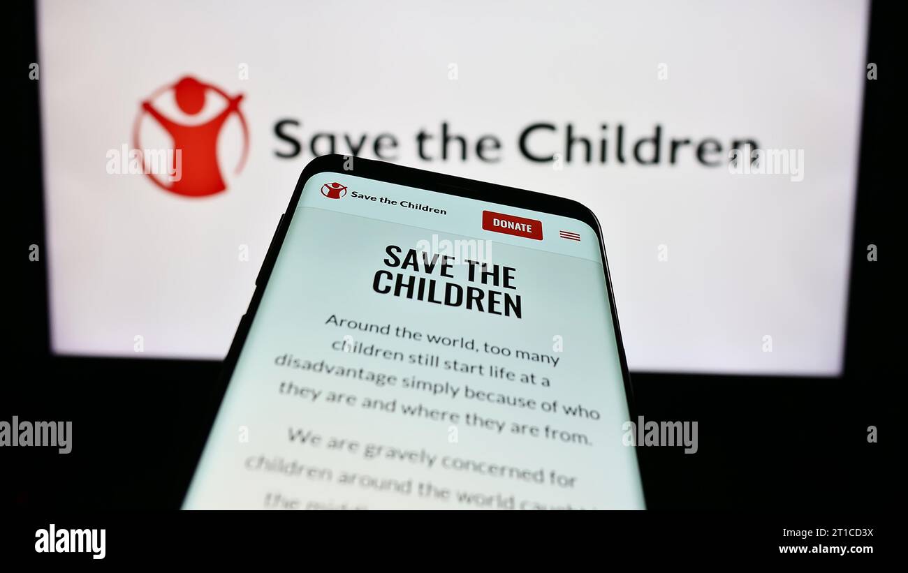 Smartphone avec le site Web de l'organisation caritative Save the Children Fund devant le logo. Effectuez le focus sur le coin supérieur gauche de l'écran du téléphone. Banque D'Images