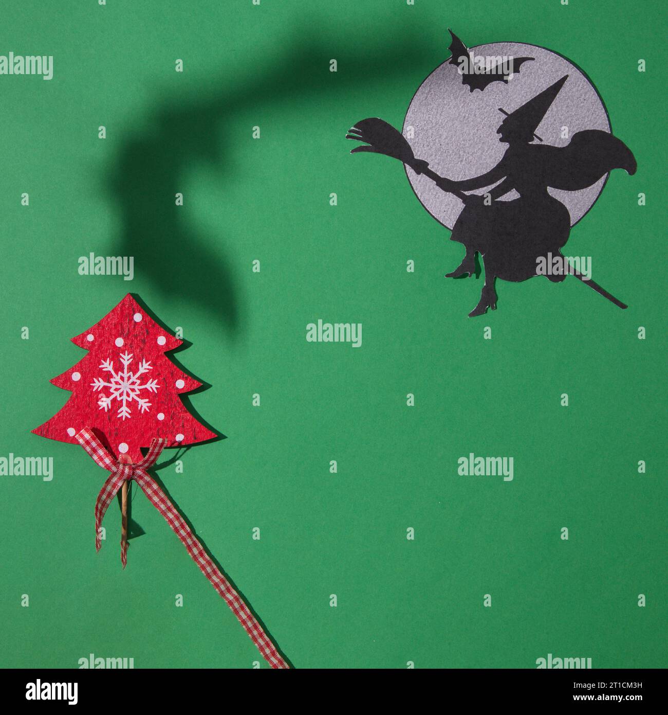 Une sorcière sur un balai vole à côté de la lune avec une chauve-souris et une ombre d'une chauve-souris au-dessus de l'arbre de Noël, sur un fond vert. Espace de copie et plat minimal Banque D'Images