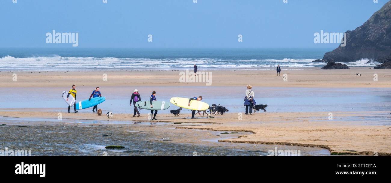 Une image panoramique de trois surfeurs et de leur moniteur de surf revenant après une leçon de surf à Mawgan Porth à Cornwall au Royaume-Uni. Banque D'Images