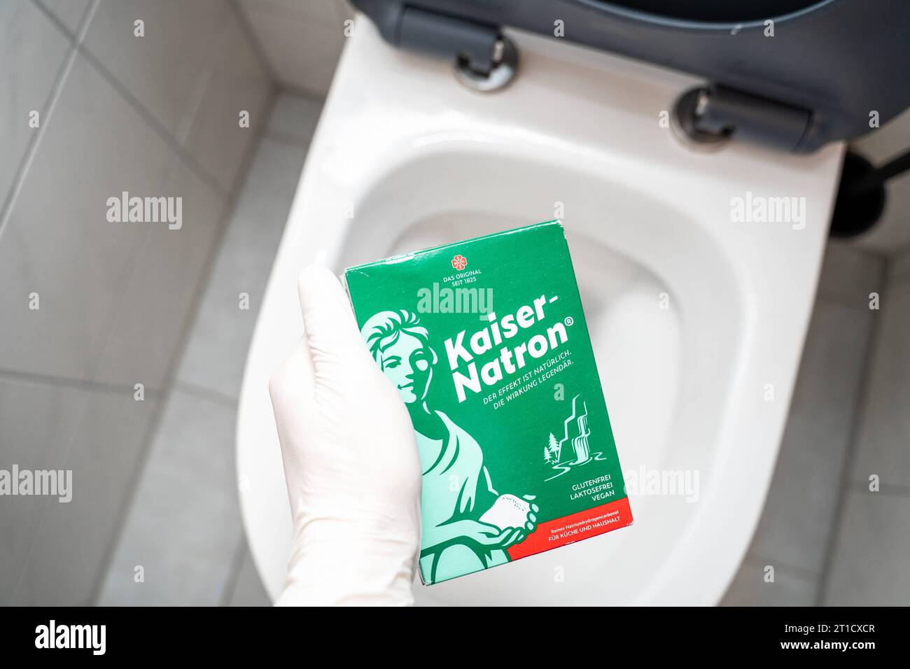 Augsbourg, Bavière, Allemagne - 29 septembre 2023 : main gantée tenant un paquet de Kaiser Natron devant une toilette. Remède maison pour le nettoyage et le débouchage *** main mit Handschuhen hält eine Packung Kaiser Natron vor eine toilette. Hausmittel zur Reinigung und zum lösen von Verstopfungen Banque D'Images
