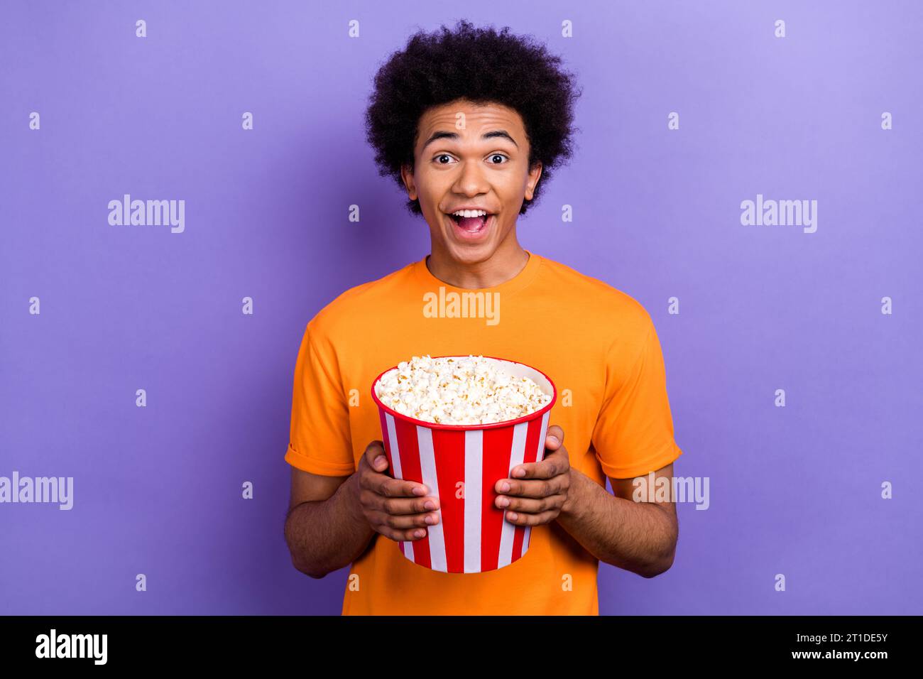 Photo de gars positif fou jeune tenir des chips de seau mangeant malsain pop corn comédie Marvel film isolé sur fond de couleur violette Banque D'Images