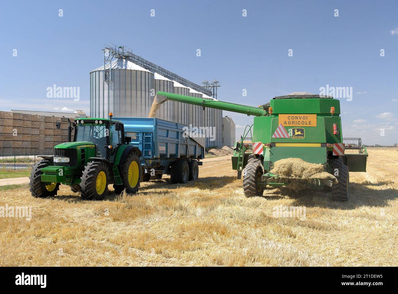 Récolte d'orge : récolte d'été dans le département de l'Essonne (région parisienne). Moissonneuse-batteuse et silos coopératifs en arrière-plan. Banque D'Images
