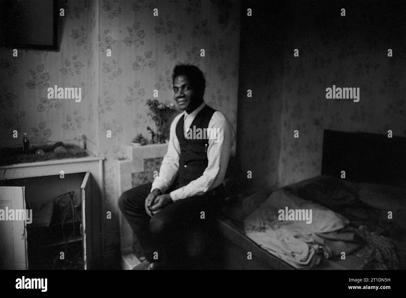 Un homme noir s'assit sur son lit dans sa maison mitoyenne victorienne pendant le nettoyage des bidonvilles et la démolition de St ann's, Nottingham, Angleterre. 1969-1970 Banque D'Images