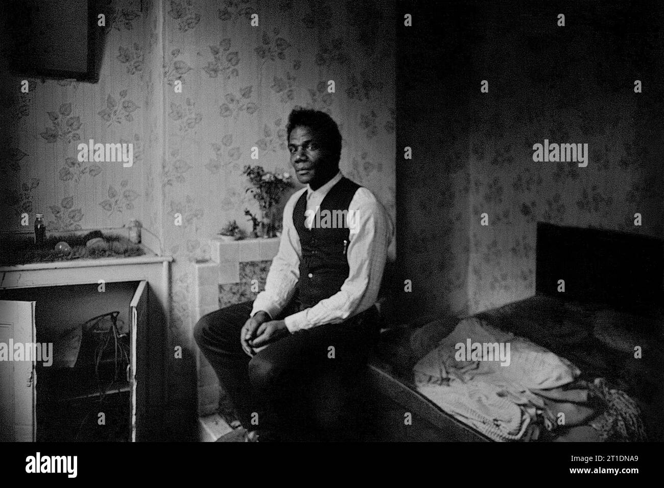 Un homme noir s'assit sur son lit dans sa maison mitoyenne victorienne pendant le nettoyage des bidonvilles et la démolition de St ann's, Nottingham, Angleterre. 1969-1970 Banque D'Images