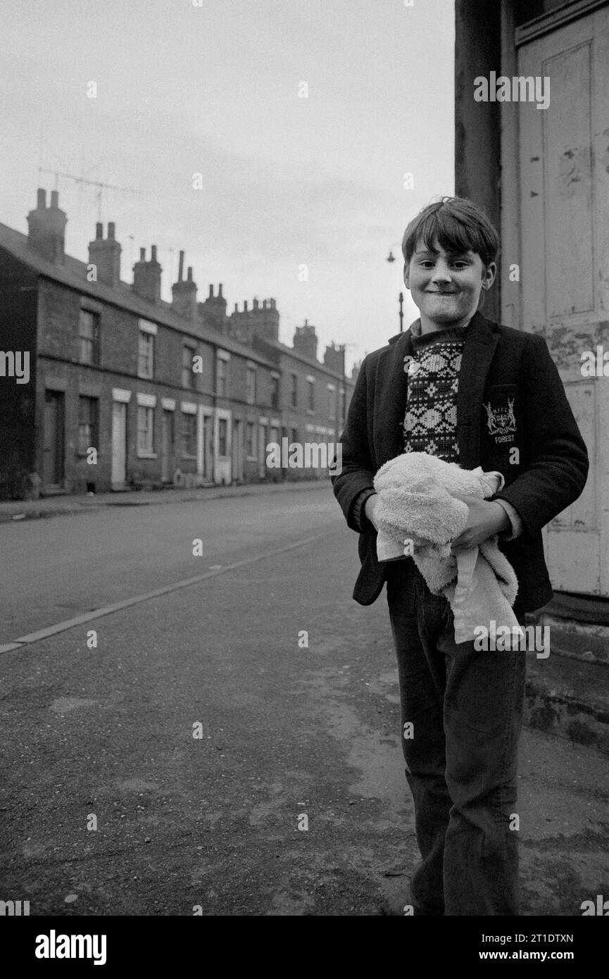 Garçon portant un blazer d'école avec un badge de la forêt de Nottingham et tenant une serviette pendant le nettoyage du bidonville de St ann's, Nottingham. 1969-1972 Banque D'Images