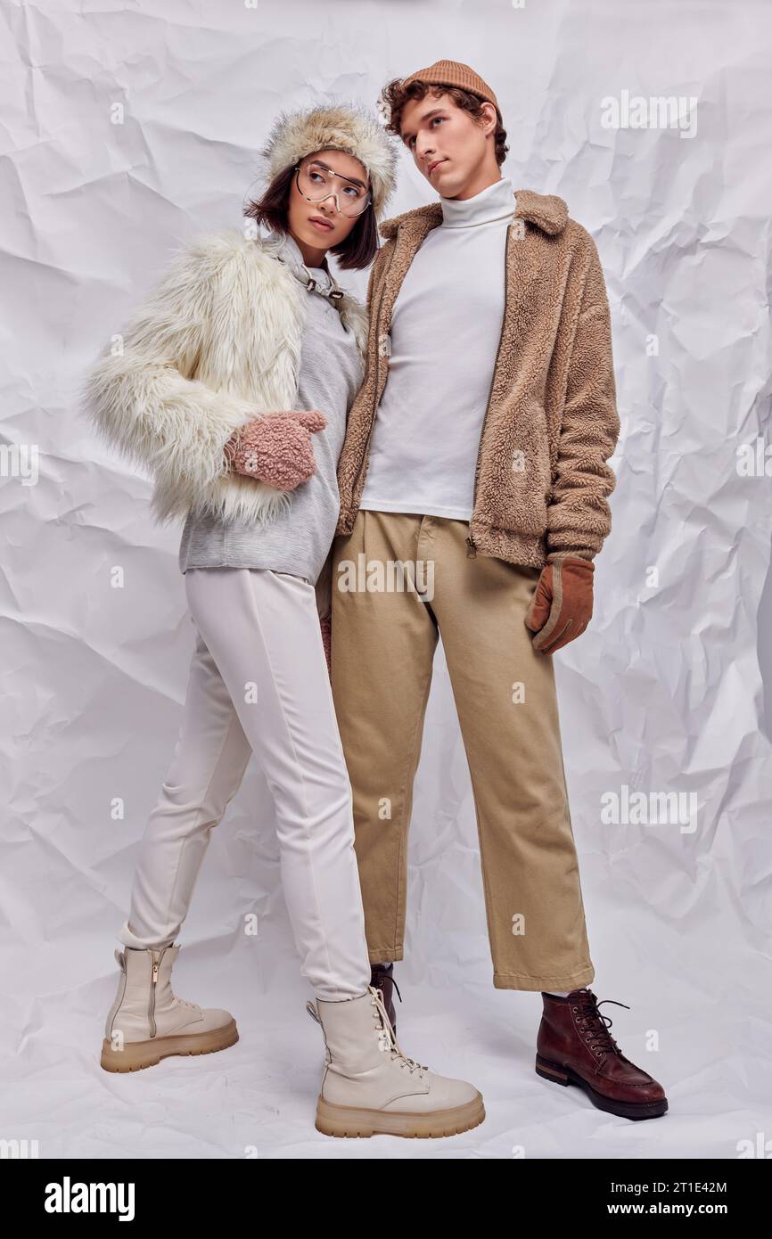 couple multiethnique dans des vêtements d'hiver à la mode regardant loin sur fond texturé blanc, style saisonnier Banque D'Images