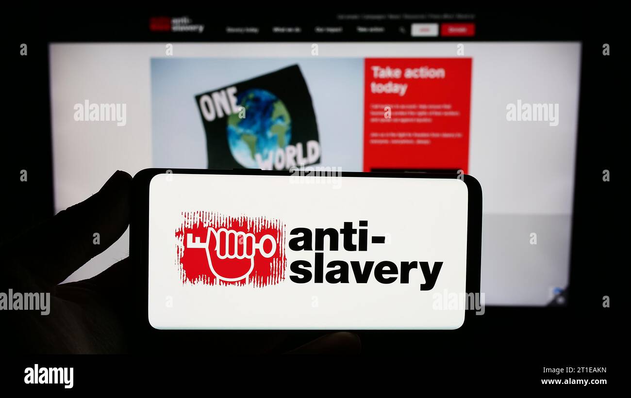 Personne tenant un smartphone avec le logo de l'organisation britannique anti-Slavery International devant le site Web. Concentrez-vous sur l'affichage du téléphone. Banque D'Images