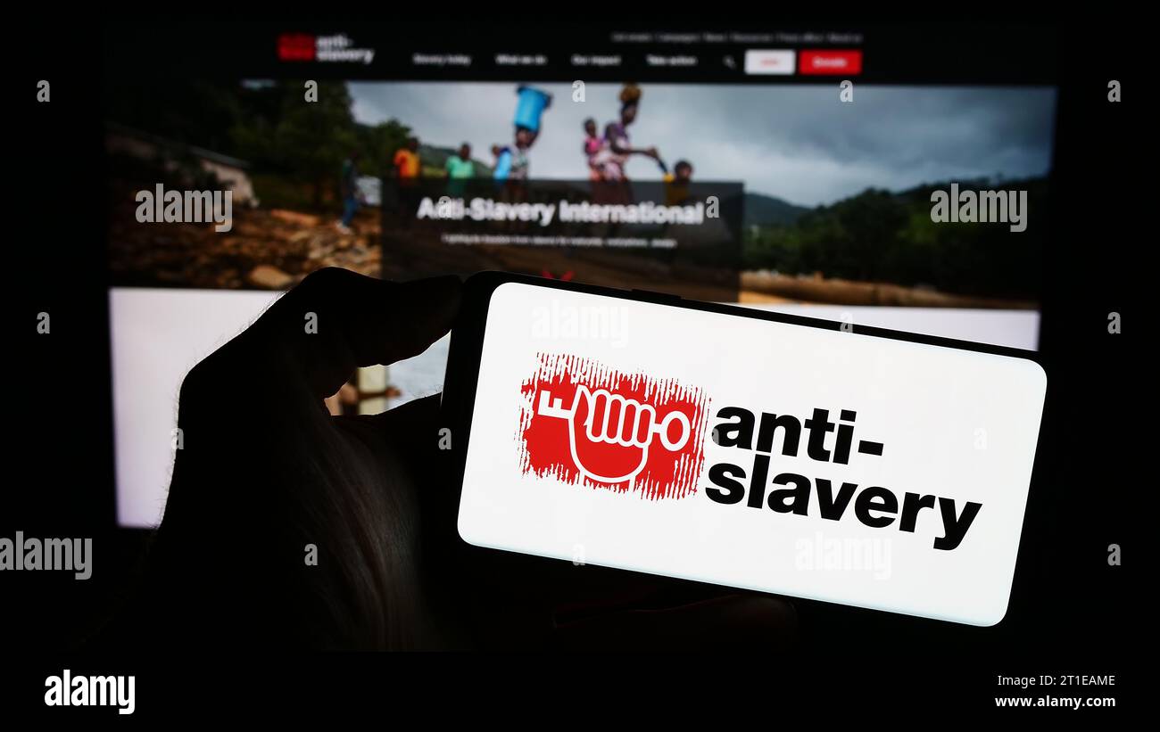 Personne tenant un téléphone portable avec le logo de l'organisation britannique anti-Slavery International devant la page Web. Concentrez-vous sur l'affichage du téléphone. Banque D'Images