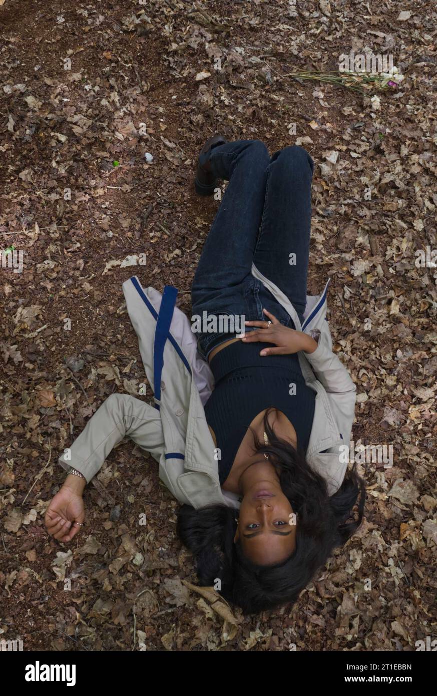 jeune femme noire portant ankh d'or couché dans les feuilles mortes d'un sol forestier Banque D'Images