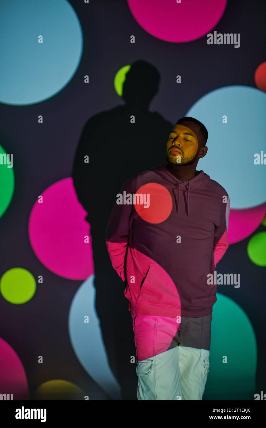 modèle masculin afro-américain à la mode avec les yeux fermés dans les lumières de projecteur numérique, concept de mode Banque D'Images