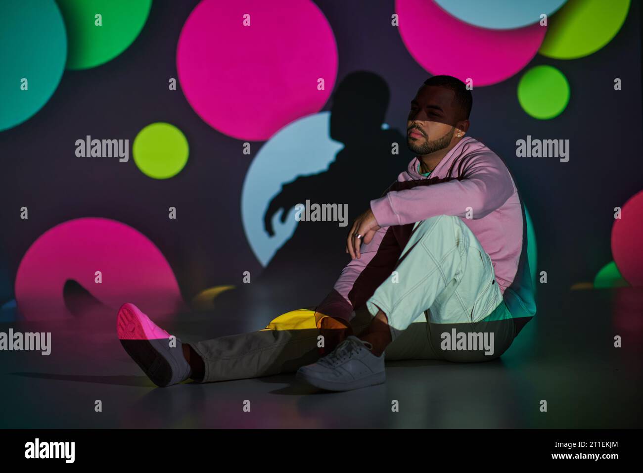 modèle masculin beau avec barbe assis sur le sol dans les lumières de projecteur numérique, concept de mode Banque D'Images