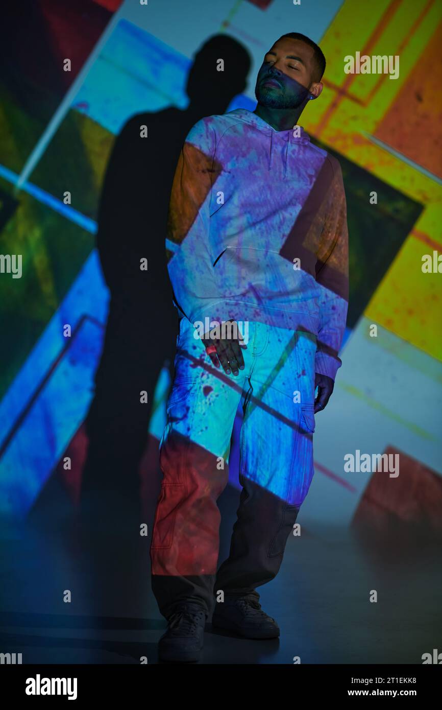 beau jeune modèle masculin en sweat à capuche rose regardant loin dans les lumières de projecteur numérique, concept de mode Banque D'Images