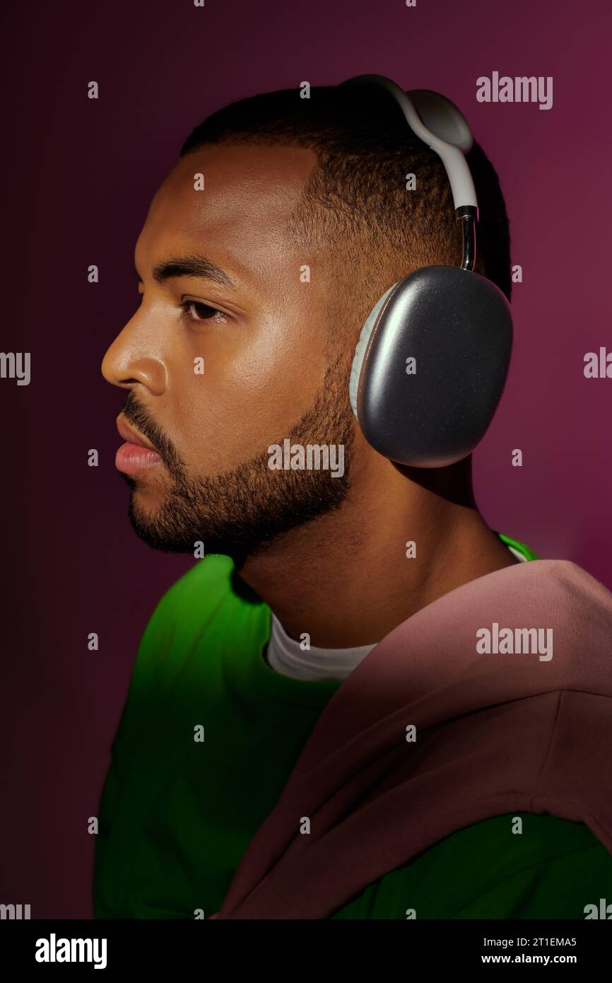 jeune modèle masculin élégant posant dans le profil avec des écouteurs sur fond violet, concept de mode Banque D'Images