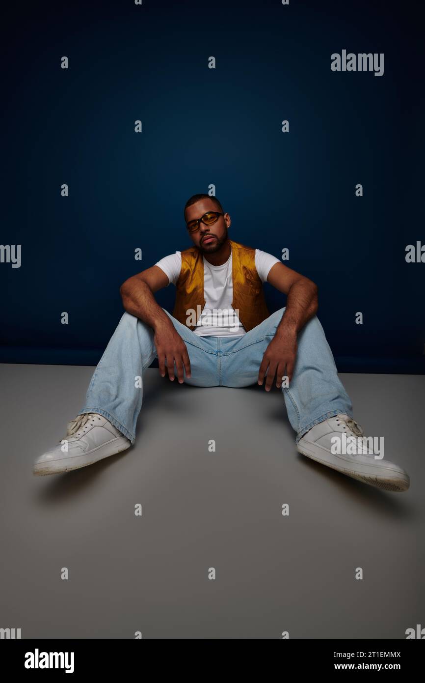 modèle masculin décontracté en gilet jaune et jeans posant sur le sol avec les bras sur les genoux, concept de mode Banque D'Images