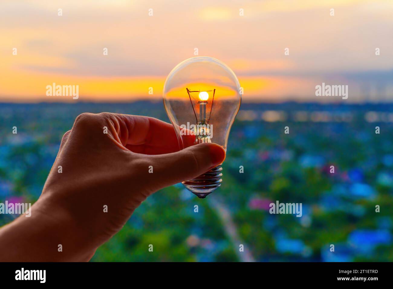 Main tenant une ampoule fusionnant avec le soleil levant, symbolisant l'aube de l'innovation technologique. Banque D'Images