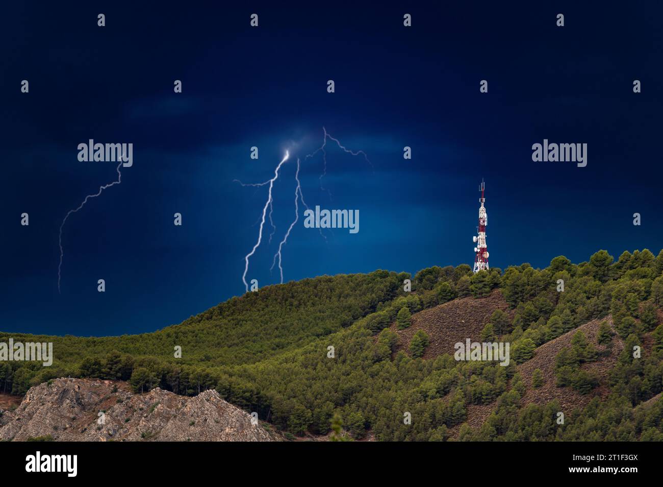 Tempête avec la foudre frappant à côté d'une grande antenne de télécommunications sur une colline avec des arbres Banque D'Images