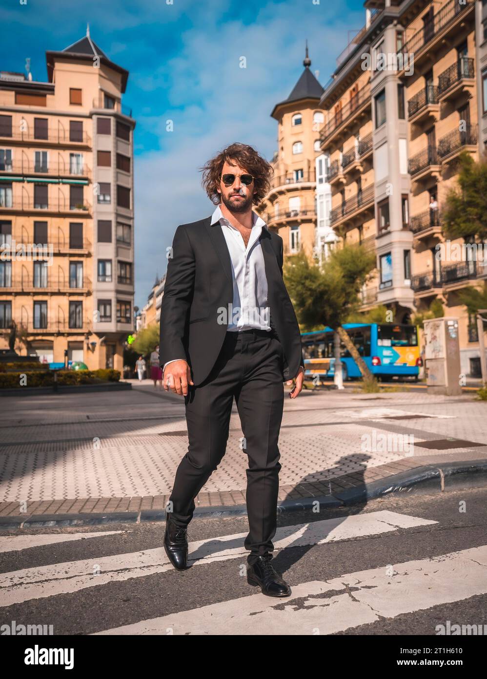 Street style un élégant costume noir, chemise blanche et lunettes de soleil. Avec un beau jeune homme caucasien aux cheveux longs dans la ville. Éditorial mode. CRO Banque D'Images