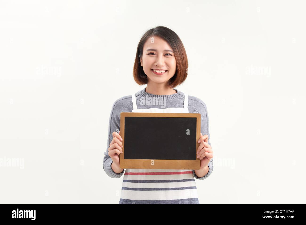 Belle femme en tablier de barista tenant un tableau noir vide sur fond blanc isolé Banque D'Images